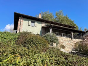 Une maison à deux étages avec une façade en pierre, un balcon doté d’une rambarde en métal et un ciel d’un bleu éclatant.