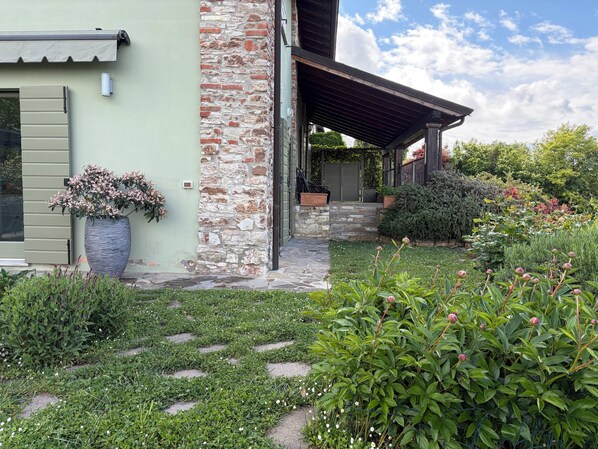 A house with a stone wall, a covered porch, and a garden with various plants and flowers.