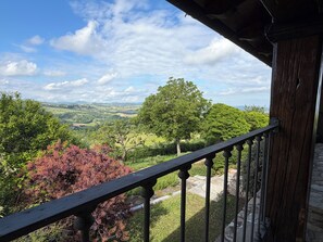 A balcony with a view of a green landscape and distant hills.