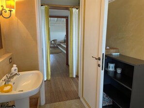 Une salle de bain avec un lavabo, un rideau de douche et une porte donnant sur une chambre.
