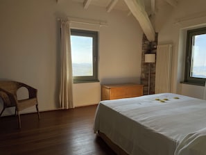 A bedroom with a wooden bed, a chair, a wooden dresser, and two windows with curtains.