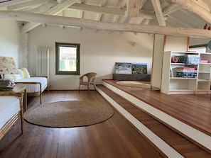A room with a bed, a chair, a woven rug, a window, and a shelf with boxes.