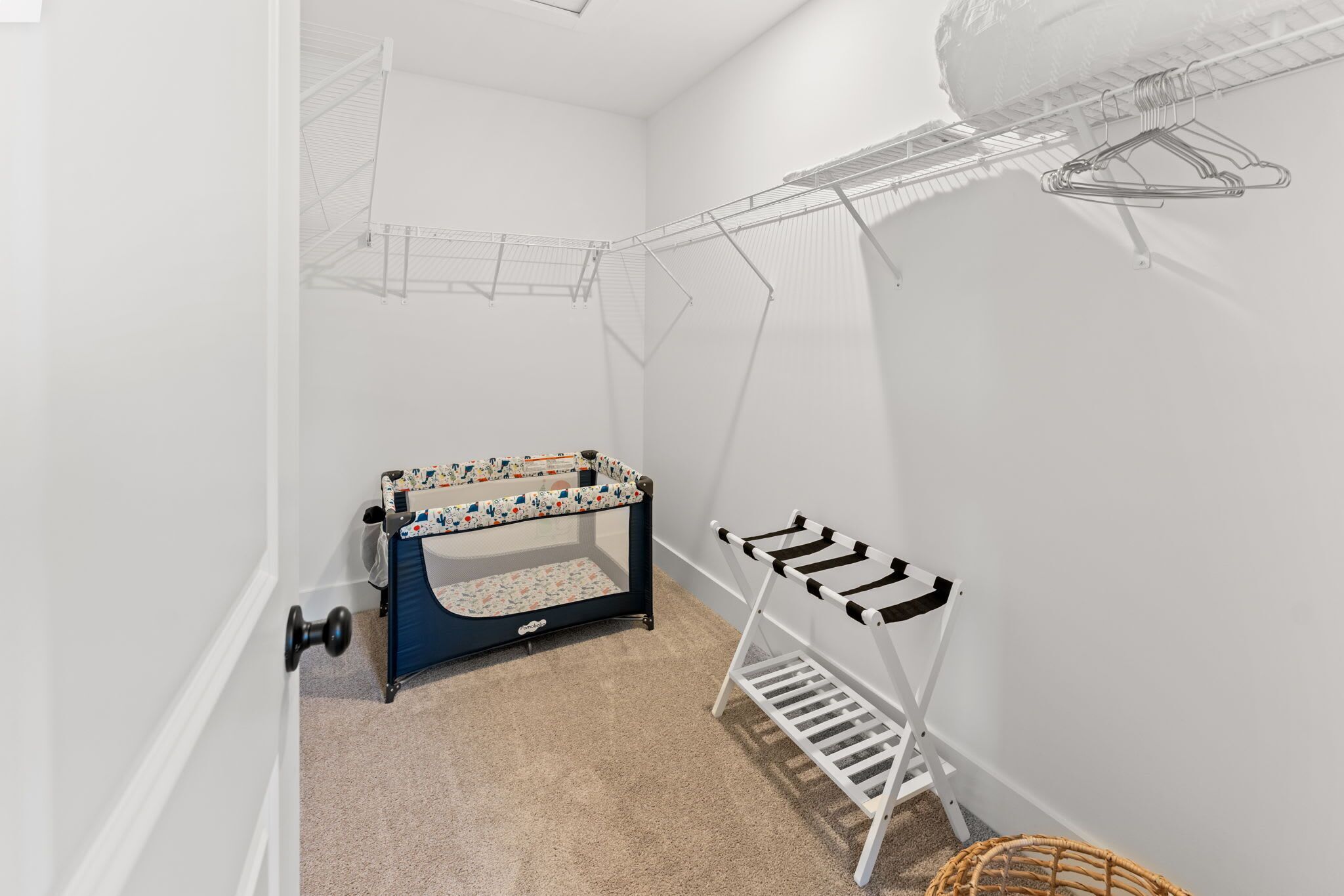 A room with a crib, a drying rack, and a basket.
