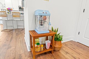 Une machine à pop-corn bleue est posée sur une table en bois, à côté d’un récipient à pop-corn, d’un pot de moutarde et d’un panier rempli de pop-corn.