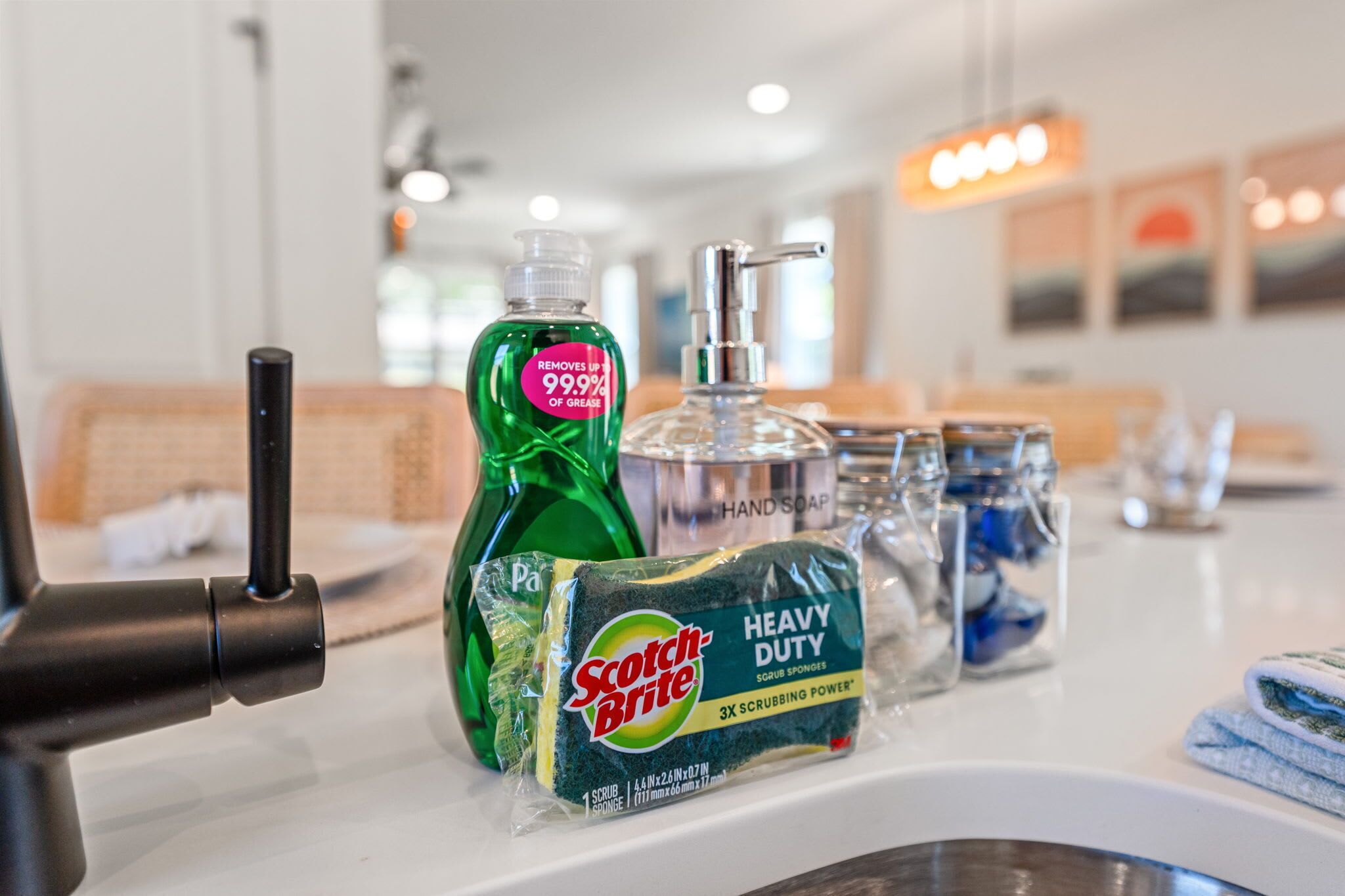 A bathroom sink with a green bottle of hand soap, a soap dispenser, a scrub sponge, and a dish soap bottle.