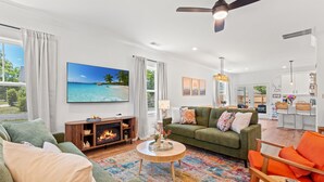 A modern living room with a fireplace, green sofas, a colorful rug, and a large beach painting. - NEW BUILD | 10 Mins to Folly | 4 BR, 10 Guests (Charleston)