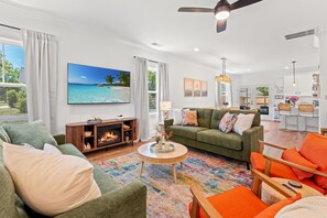 A living room with a fireplace, green sofas, a colorful rug, and a large beach painting. - NEW BUILD | 10 Mins to Folly | 4 BR, 10 Guests (Charleston)