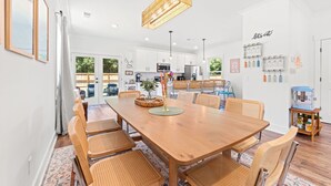 A modern kitchen with white cabinets, a wooden dining table, wicker chairs, and a hanging light fixture. - NEW BUILD | 10 Mins to Folly | 4 BR, 10 Guests (Charleston)