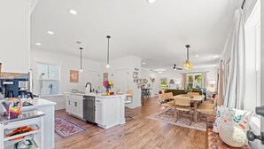 A spacious kitchen with white cabinets, a central island, and a dining area with a wooden bench. - NEW BUILD | 10 Mins to Folly | 4 BR, 10 Guests (Charleston)