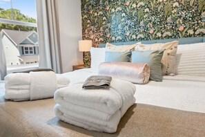 A neatly made bed with rolled towels, a floral wallpaper, and a view of houses outside. - NEW BUILD | 10 Mins to Folly | 4 BR, 10 Guests (Charleston)
