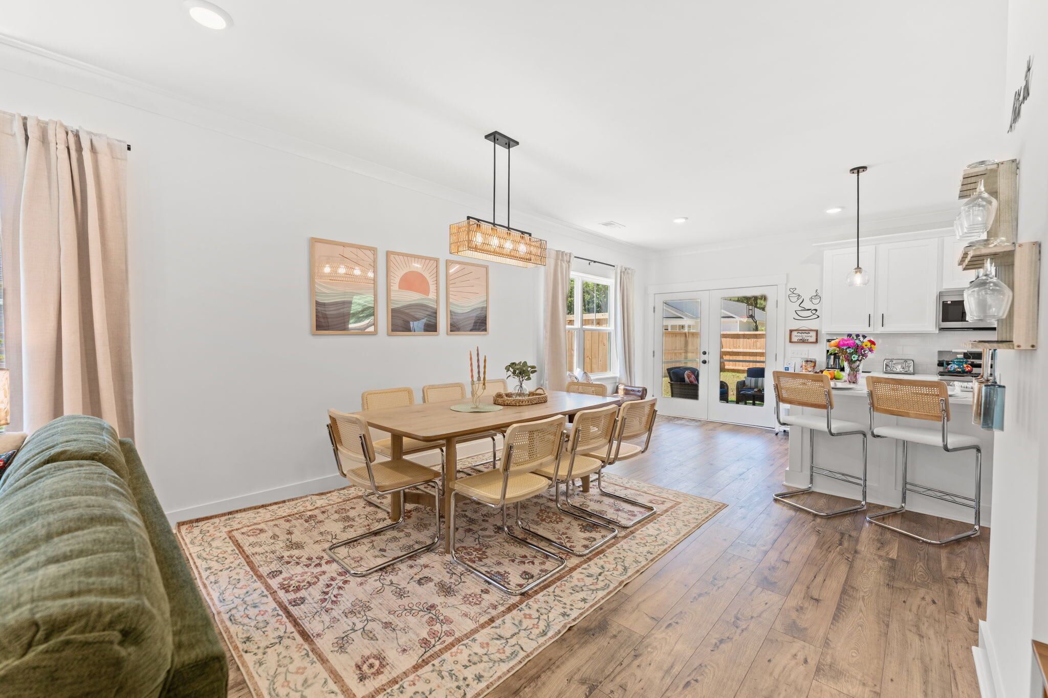 A modern kitchen with white cabinets, a dining area with a wooden table and chairs, and a kitchen island with bar stools.