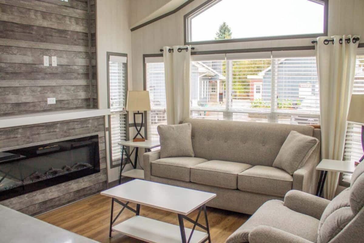 A living room with a fireplace, a sofa, a table, and large windows with curtains.