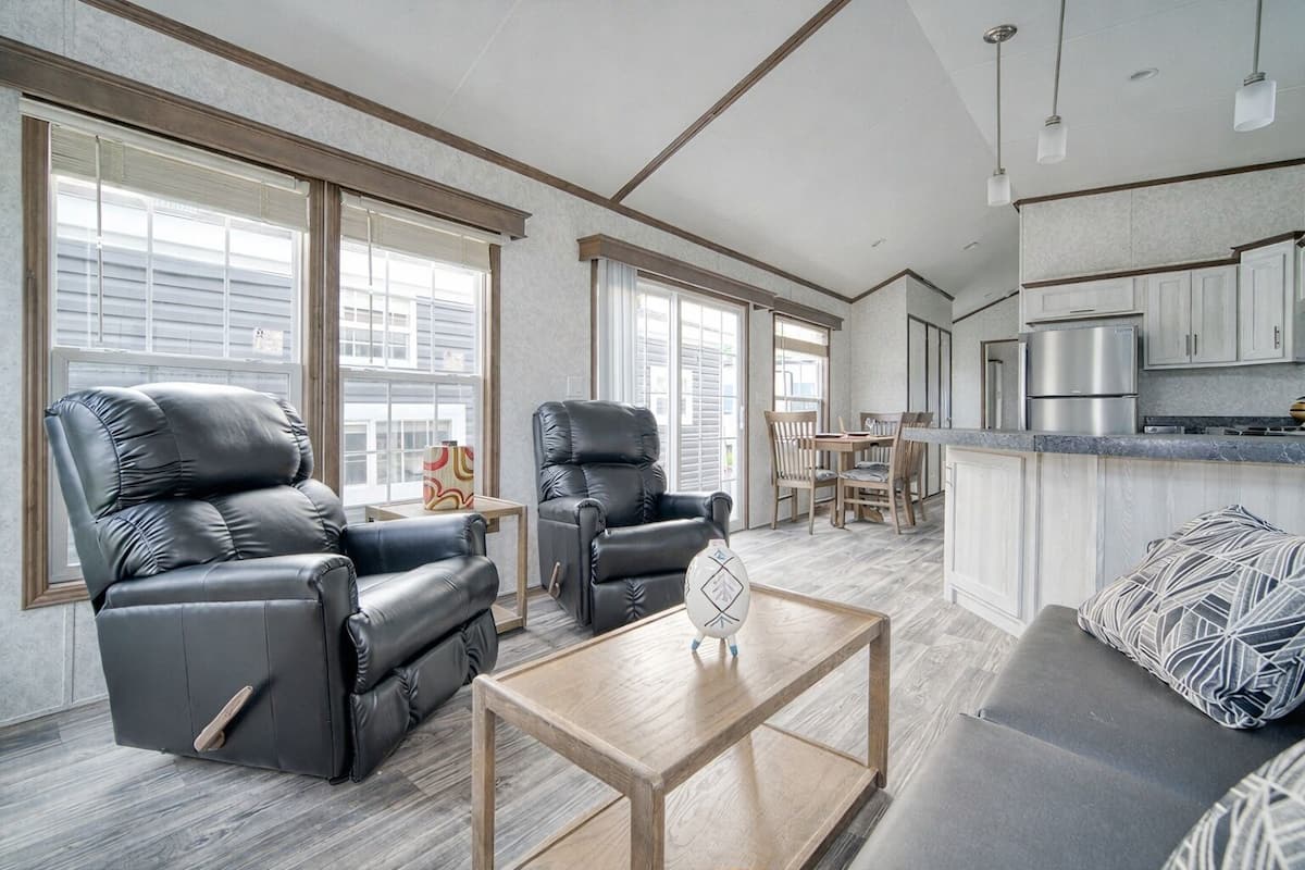 A spacious living area with leather recliners, a wooden coffee table, and a kitchen with modern appliances.