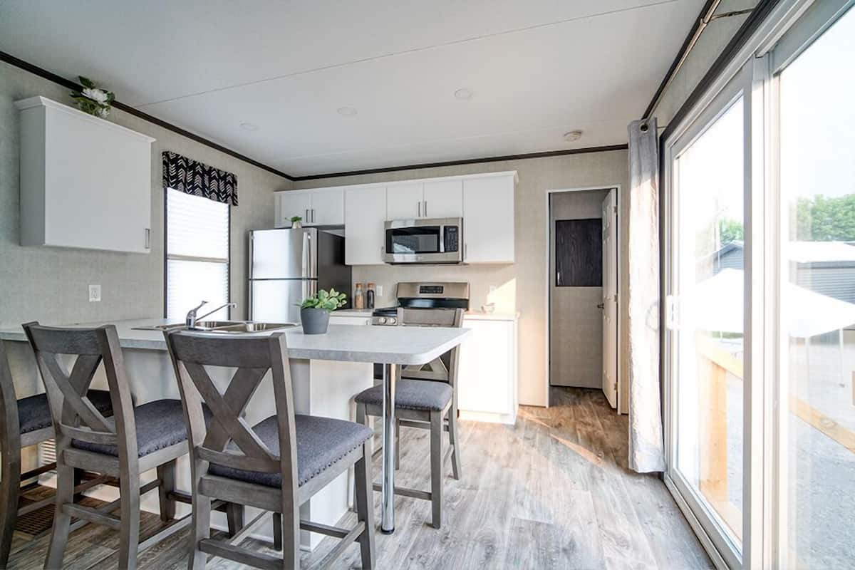 A modern kitchen with white cabinets, a microwave, a refrigerator, and a dining area with grey chairs.