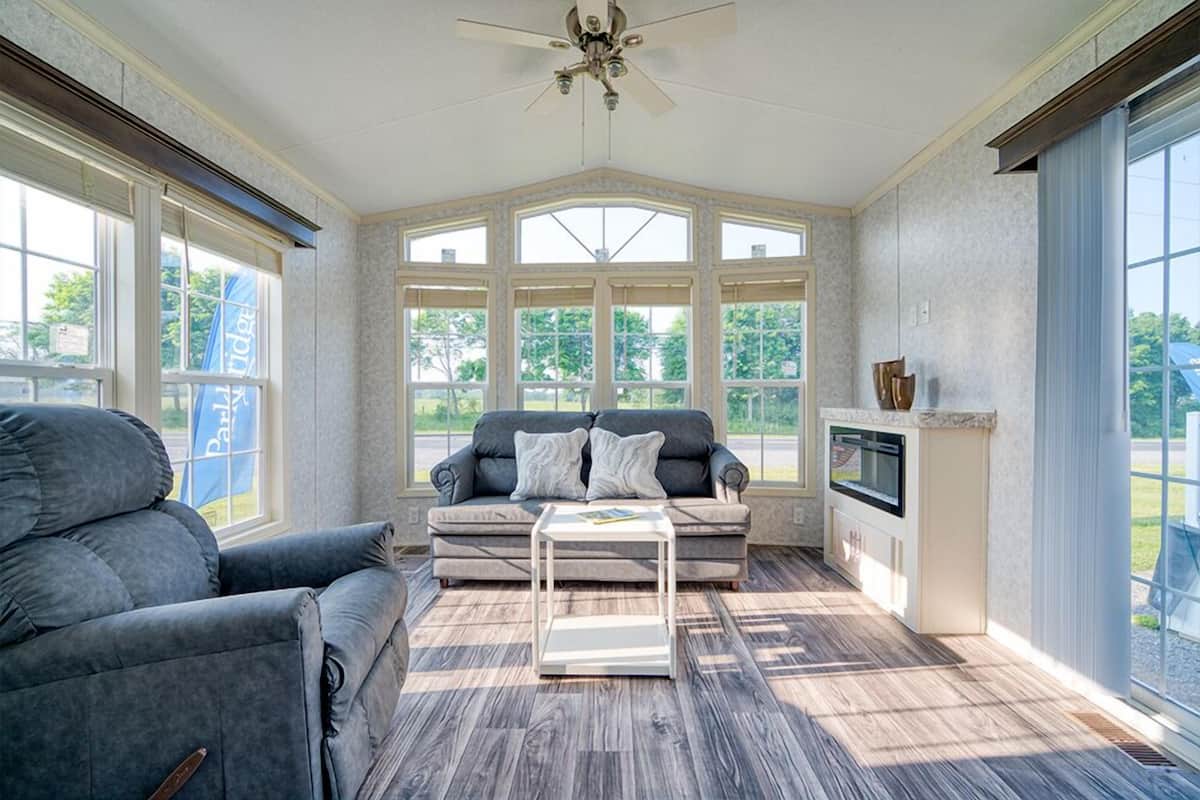 A sunroom with a ceiling fan, a gray sofa, a white coffee table, and a fireplace.