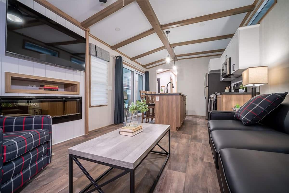 A modern kitchen with wooden beams, a dining area with a table and chairs, and a living area with a sofa and a TV.