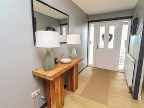 A hallway with a wooden console table, two lamps, a mirror, and a door with a wreath. - Tigh-na-mara Retreat (Berwick-upon-Tweed)