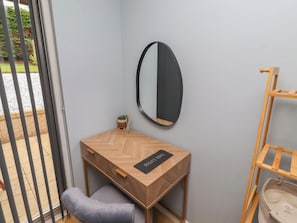 Ein Zimmer mit Schreibtisch aus Holz, einem Stuhl, einem Spiegel und einer kleinen Topfpflanze.