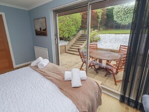 A bedroom with a bed, a view of a patio with a table and chairs, and a painting on the wall. - Tigh-na-mara Retreat (Berwick-upon-Tweed)