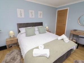 A neatly made bed with pillows, a bedside table with a lamp, a desk with a chair, and a door. - Tigh-na-mara Retreat (Berwick-upon-Tweed)