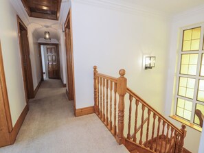 A hallway with wooden doors, a carpeted floor, and a wooden staircase with a balustrade. - The Boat Yard Apartment (Porthmadog)