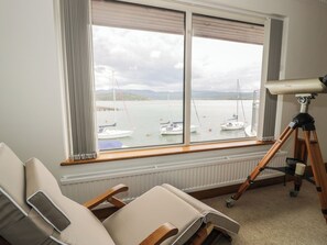 A room with a large window overlooking a marina, a telescope, and two reclining chairs. - The Boat Yard Apartment (Porthmadog)