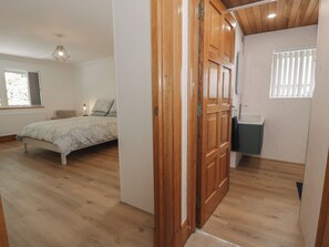A bedroom with a bed, a wooden door, a window, and a bathroom with a sink. - The Boat Yard Apartment (Porthmadog)