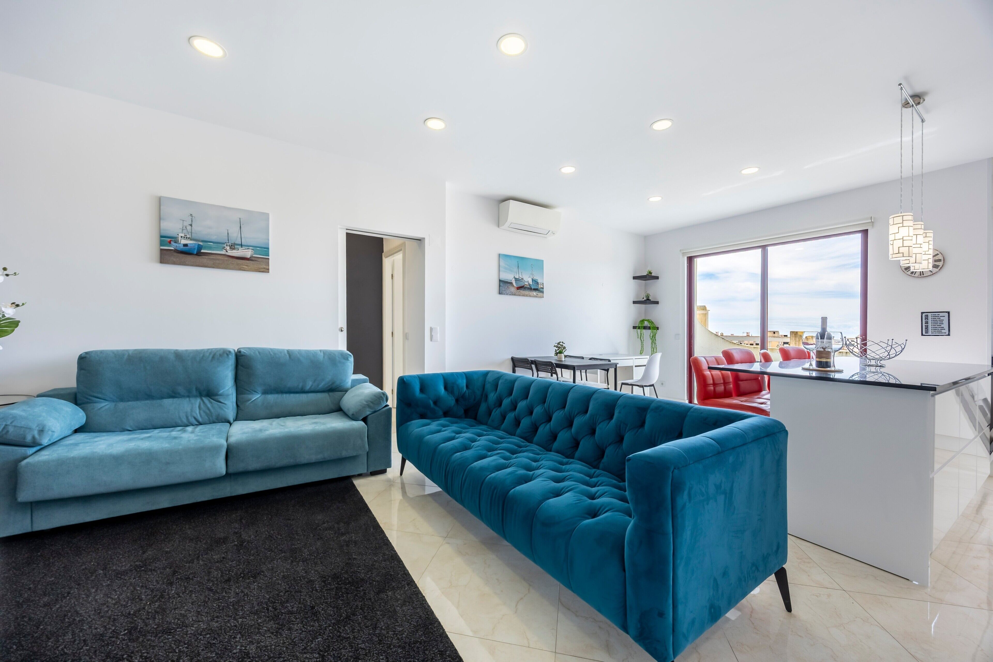Ein modernes Wohnzimmer mit einem blauen Sofa, einem Essbereich mit einem roten Stuhl und einer Kücheninsel.