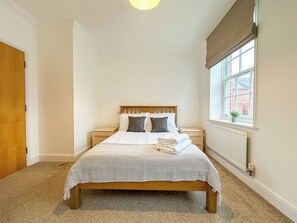 Un dormitorio con cama, mesitas de noche, ventana con vistas y un radiador.