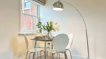 A room with a dining table, two chairs, a vase with flowers, a blue sofa, and a floor lamp.