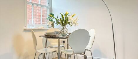 Une pièce comprenant une table à manger, deux chaises, un vase avec des fleurs, un canapé bleu et un lampadaire.