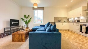 A modern living room with a sofa, a TV, a plant, and a window. - Cosy & Stylish Canterbury Apartment | Free Parking (Canterbury)