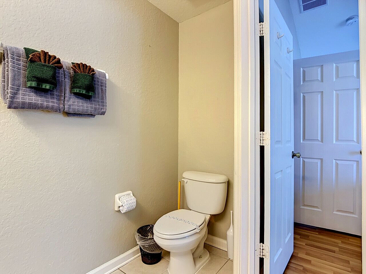A small bathroom with a toilet, a trash can, and a towel rack with folded towels.