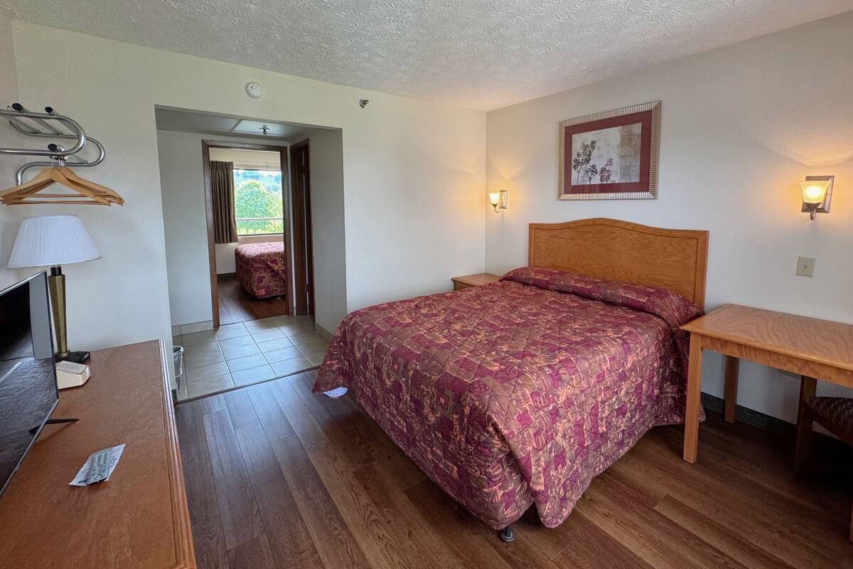A bedroom with a bed, bedside table, lamp, and a view of the outdoors.