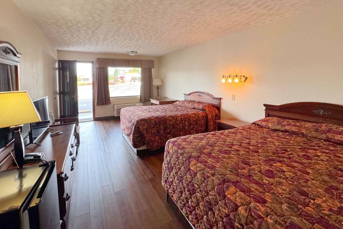 A hotel room with two beds, a desk with a lamp, a TV, and a window with curtains.