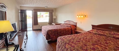 A hotel room with two beds, a desk with a lamp, a TV, and a window with curtains.