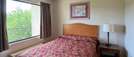 A hotel room with a bed, a window with curtains, a bedside table with a lamp, and a framed picture on the wall.