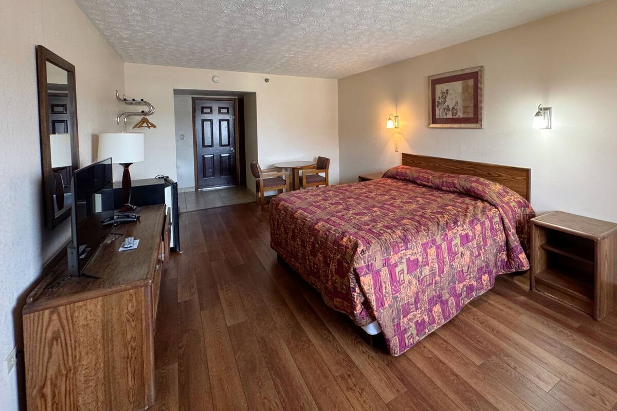 A hotel room with a bed, desk, chair, TV, and a door leading to another room.