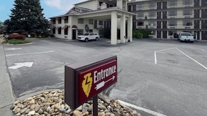Entrada de hotel con un cartel, un estacionamiento y un edificio de varios pisos.