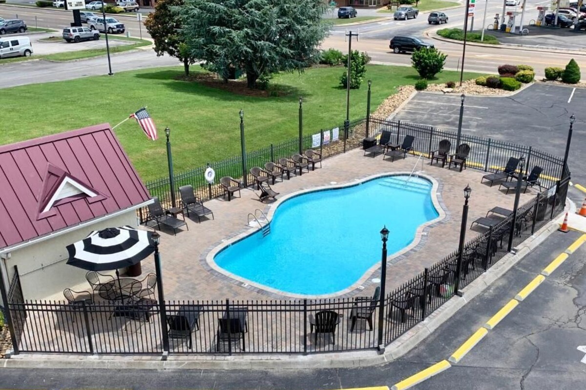 A swimming pool surrounded by a fence, with outdoor seating and a flagpole.