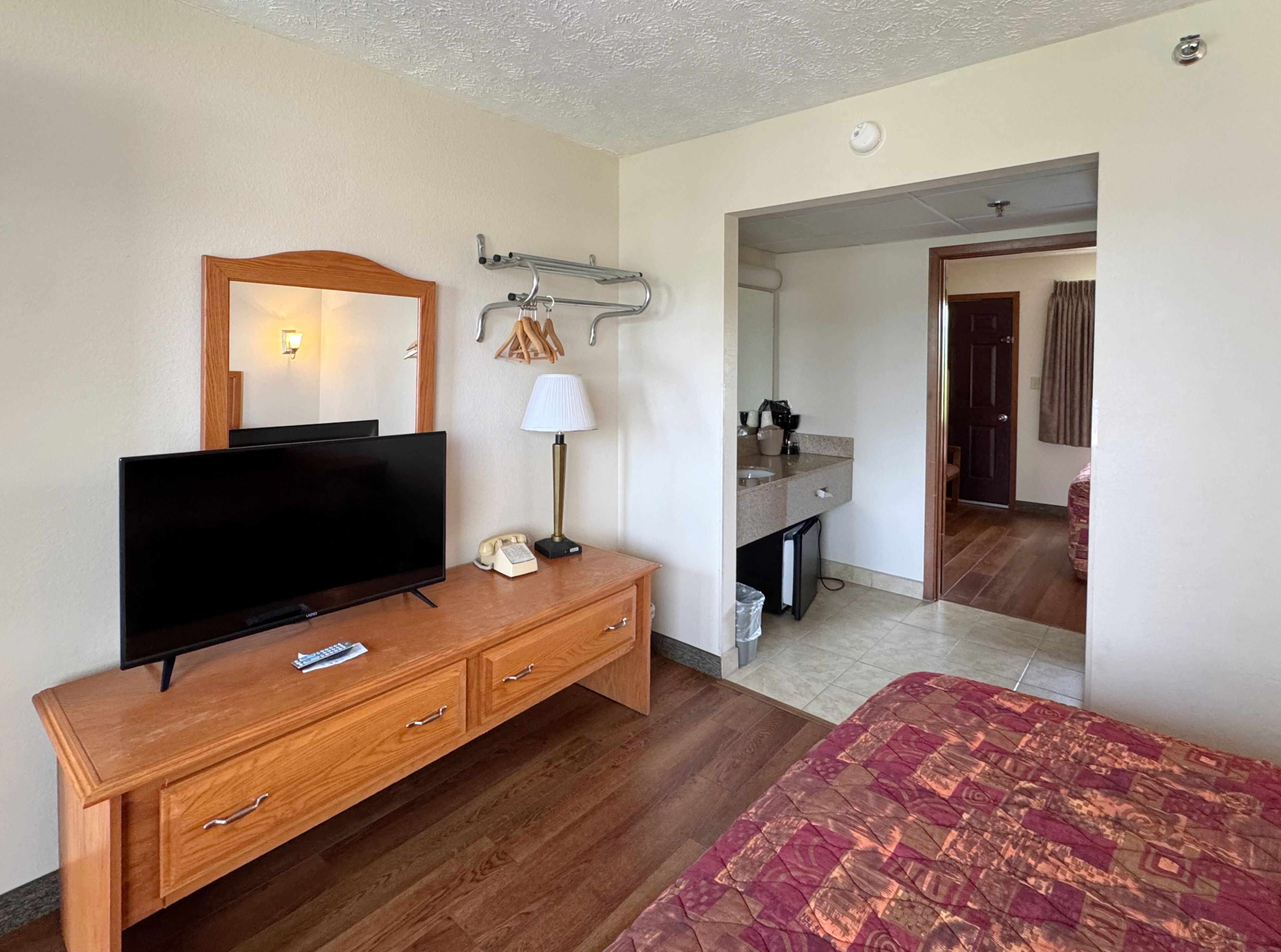 Quarto de hotel com penteadeira de madeira, televisão, candeeiro, espelho e cama.