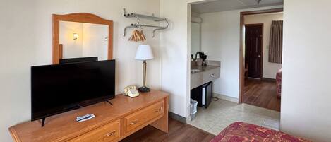 A hotel room with a wooden dresser, a television, a lamp, a mirror, and a bed.