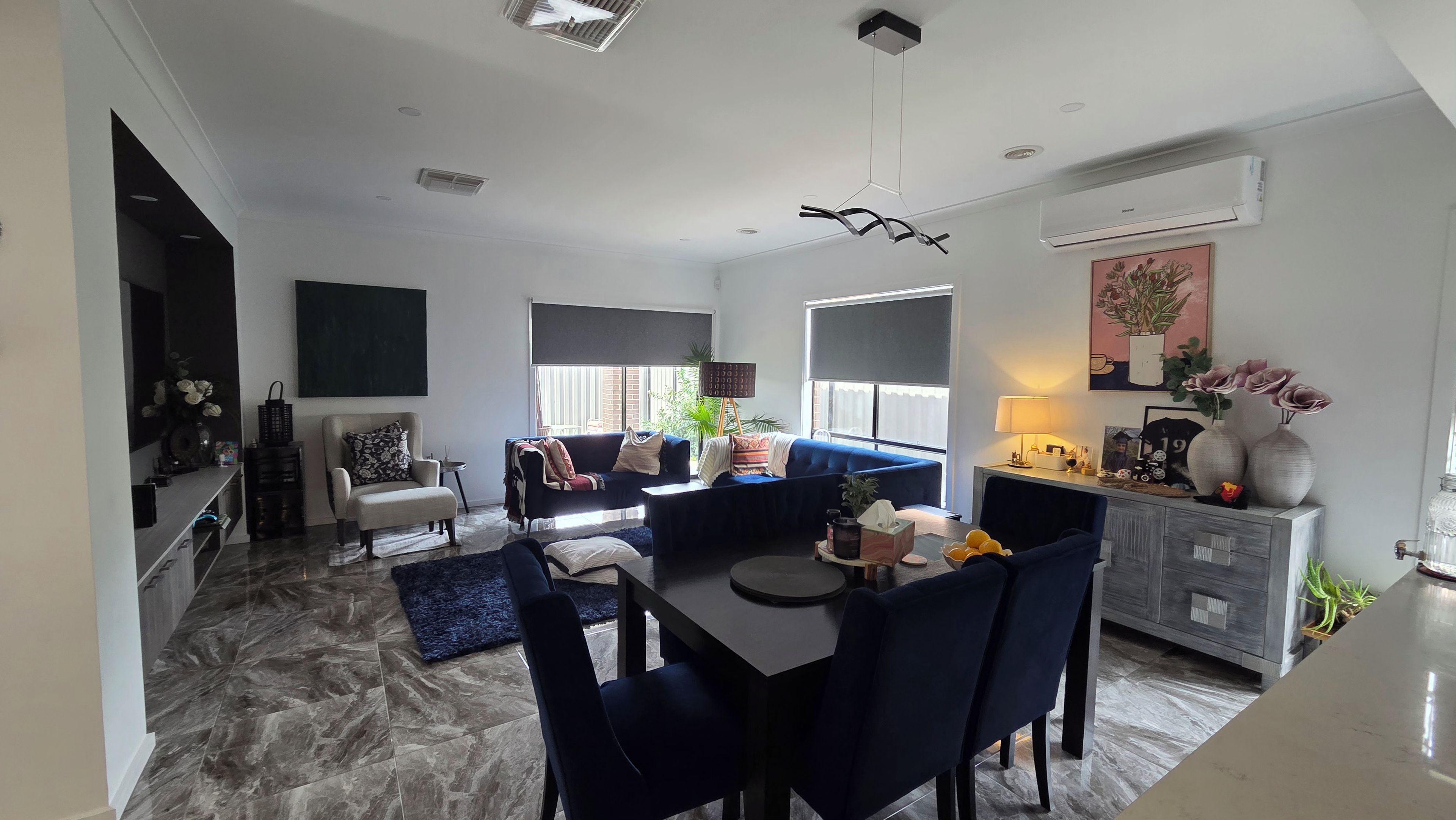 A modern living room with a dining area, a sofa set, a coffee table, and a TV mounted on the wall.
