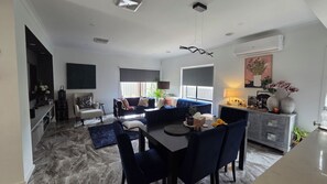 A modern living room with a dining area, a sofa set, a coffee table, and a TV mounted on the wall.