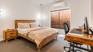 Une chambre à coucher avec un lit en bois, des tables de chevet, un bureau avec un ordinateur et un mur en briques.