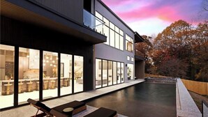 Un edificio moderno con amplios ventanales, una piscina y mobiliario exterior.