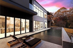Un edificio moderno con amplios ventanales, una piscina y mobiliario exterior.