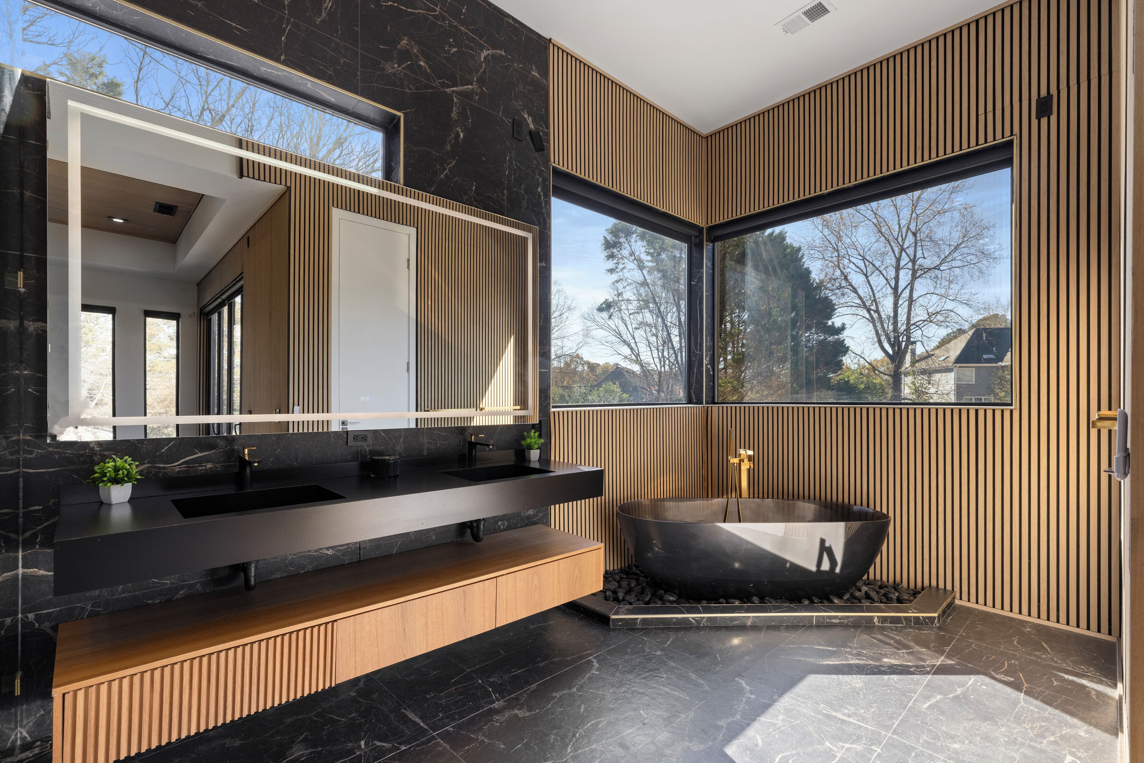 Un baño moderno con lavamanos negro, tocador de madera, un espejo grande y una bañera independiente.