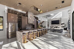 A modern kitchen with a marble island, stainless steel appliances, and a bar area with stools.