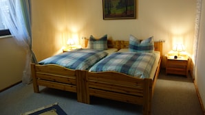 A double wooden bed with plaid bedding, two bedside tables with lamps, a painting on the wall, and a window with sheer curtains.